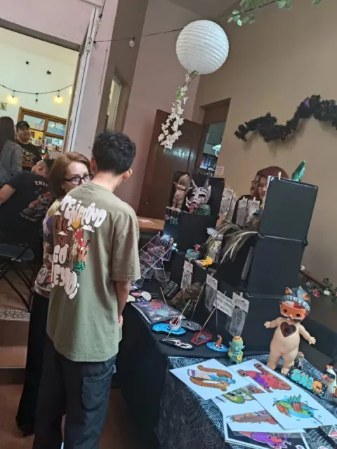 Visitantes recorriendo un stand de la feria de creadores El Fucking Hype, con art toys, ilustraciones y calcomanías sobre la mesa